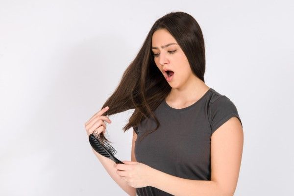 alopecia por tracción - mujer sujetándose el cabello con una mano mientras mira con preocupación el cepillo en la otra