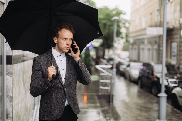 Cómo envejece nuestro pelo - hombre en la calle con un paraguas bajo la lluvia mientras llama por teléfono