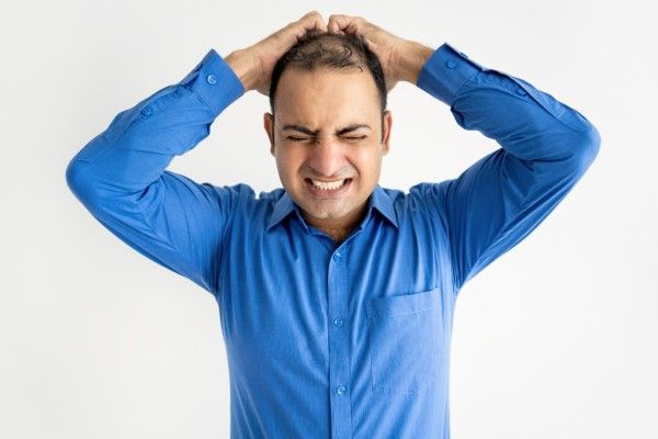 salud mental - hombre agarrando el poco cabello que le queda en la cabeza con cara de dolor