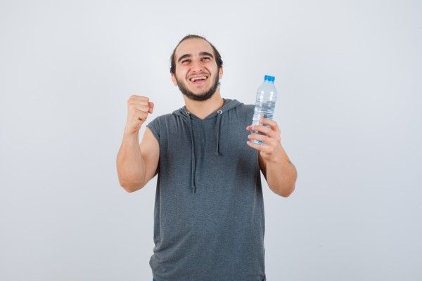 Fumar aumenta la caída del pelo - hombre joven alegre con entradas en el cabello sujetando un botellín de agua