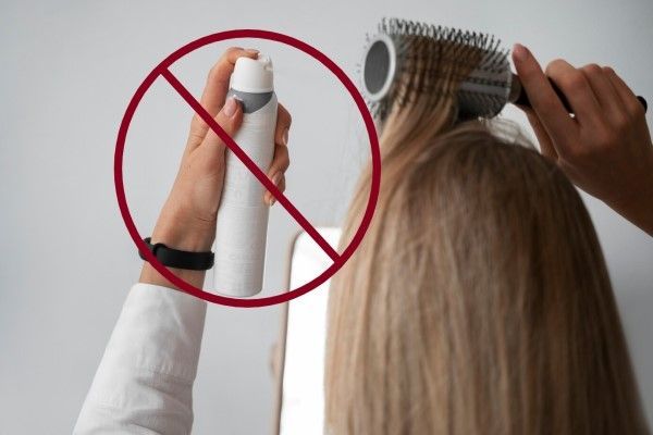 mujer usando un spray sobre su cabello con la señal de prohibido por encima