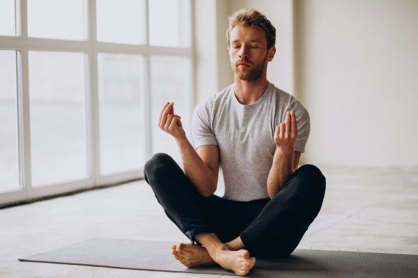 hombre realizando meditación sentado en una esterilla en el suelo