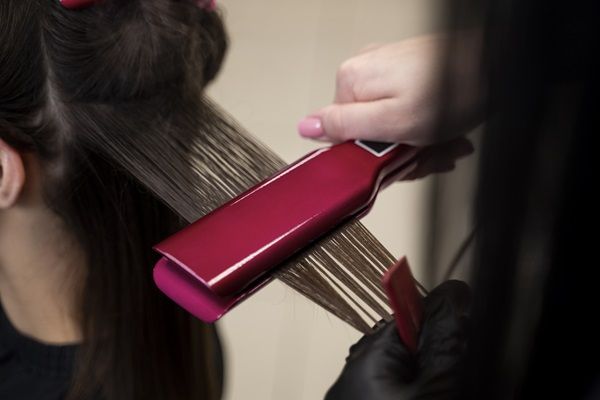 Estilista alisando el cabello de una mujer con una plancha para el cabello