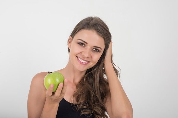 Nutrición para el pelo - Mujer sosteniendo una manzana muy feliz al tener su cabello sedoso, brillante y nutrido