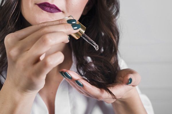 Biotina para el pelo - Mujer aplicando gotas de vitamina B7 y nutrientes en su cabello para revitalizarlo
