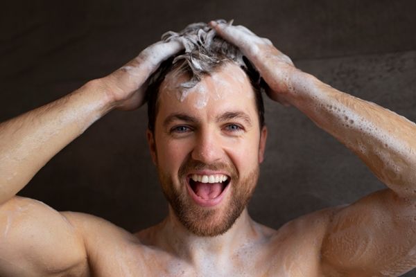Champús para el crecimiento del pelo - Hombre contento lavando su cabello con el mejor champú, para fortalecerlo