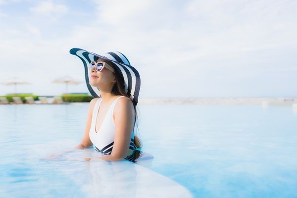 Revitalizar el pelo después del verano - Mujer usando un sombrero mientras disfruta de las vacaciones en la piscina, para proteger el cabello del sol