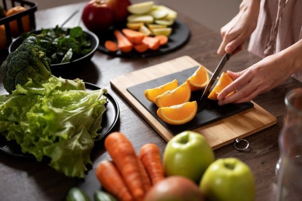 Mujer cortando frutas y hortalizas para comer sano, con muchas vitaminas y nutrientes