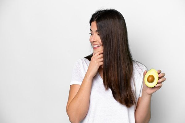 Mujer feliz sosteniendo un aguacate, que posee muchas vitaminas y minerales para nutrir el cabello