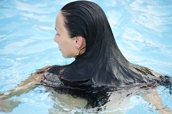 Mujer con el cabello suelto bañándose en la piscina, para evitar causarle daño con una trenza o moño