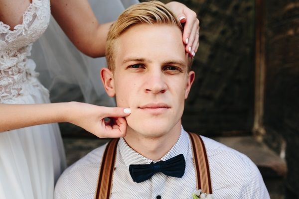 Esposa acariciando la cara de su esposo, que luce un corte de cabello formal y elegante el día de su boda