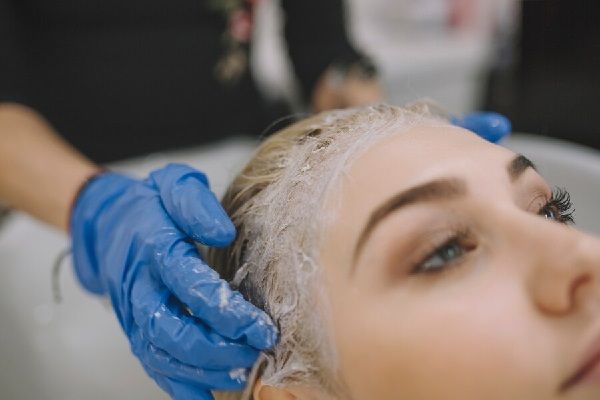 Crecer el pelo - Estilista dando masajes en el cabello de una mujer para estimular su crecimiento mientras aplica el tratamiento capilar