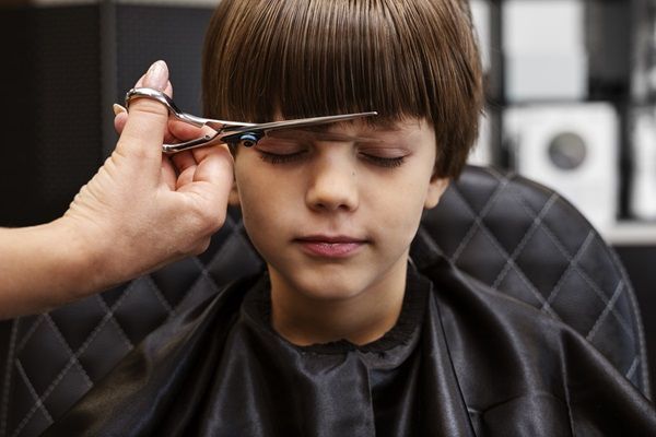 Cortes de pelo para cara redonda - Estilista cortando el cabello de un niño con cara redonda, para darle un look más estilizado