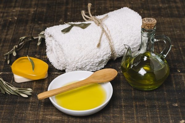 Recipiente con líquido extraído de las aceitunas, toalla y esponja para hacer una mascarilla capilar que revitaliza el cabello 