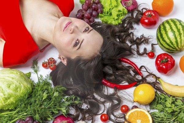 Mujer con su cabello largo y saludable acostada sobre alimentos que ayudan a nutrir y aportar nutrientes para el crecimiento capilar