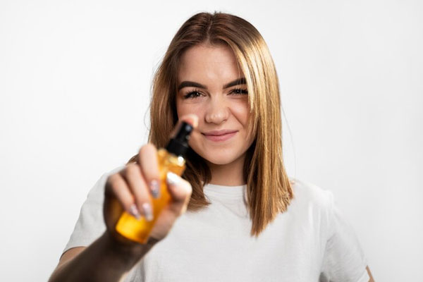 Protector solar - Joven de pelo corte y teñido sostiene un producto capilar en spray frente a la cámara 