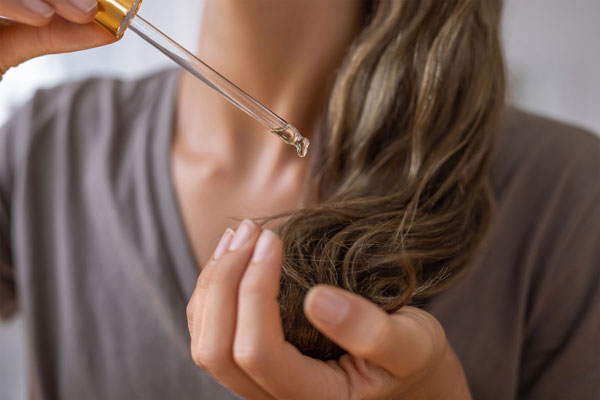 Aceite de ricino para el pelo - Mujer emplea un pequeña cantidad de aceite de castor para hidratar su melena