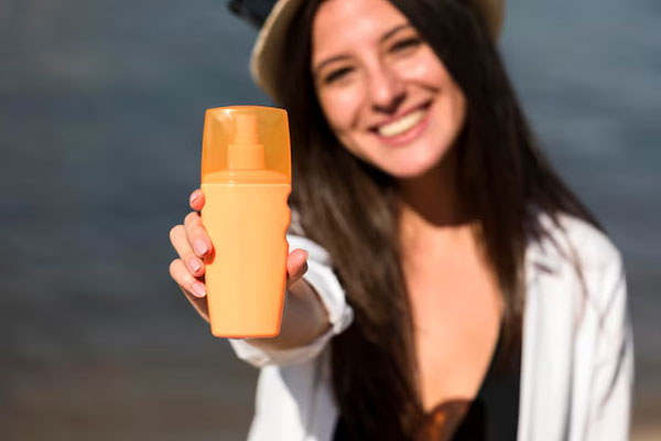 Protector solar - Mujer sostiene un spray de frasco naranja para incentivar el cuidado capilar 