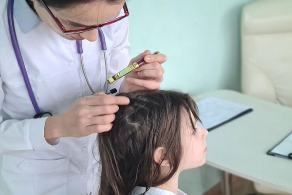 Dermatóloga examina y evalúa con detenimiento el cuero cabelludo de una niña 