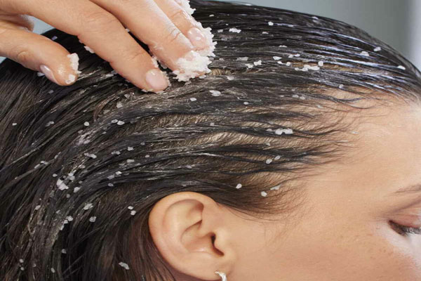 Exfoliantes capilares - Mujer aplica de manera uniforme las micropartículas de un exfoliante para optimizar el cuidado de su cuero cabelludo