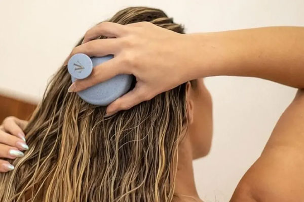 Mujer con mechas usa un masajeador manual para esparcir una mascarilla casera