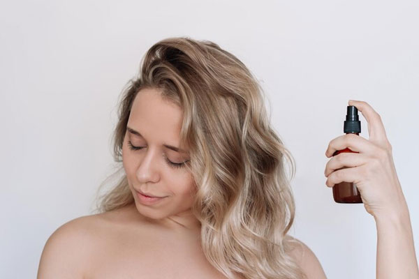 Joven rubia con cabello teñido aplica una solución en spray para reforzar la hidratación de su melena en seco 