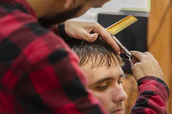 Estilista realizando un corte de cabello con mechones largos a un cliente masculino, para disimular la alopecia que presenta