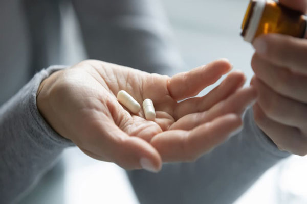 Aceite de ricino para el pelo - Mujer sostiene dos cápsulas de Minoxidil en pastillas para mejorar la oxigenación del cuero cabelludo 