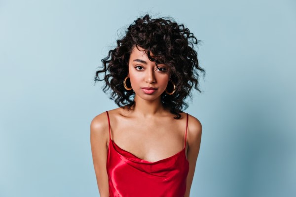 Vista frontal de una elegante mujer con la melena rizada con un vestido de tirantes rojo