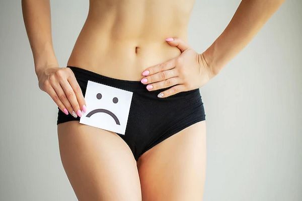 recuperar el pelo del pubis - imagen de la parte inferior del vientre de una mujer con una pantaleta negra con la mano poniendo un dibujo de una cara disgustada sobre la zona del pubis