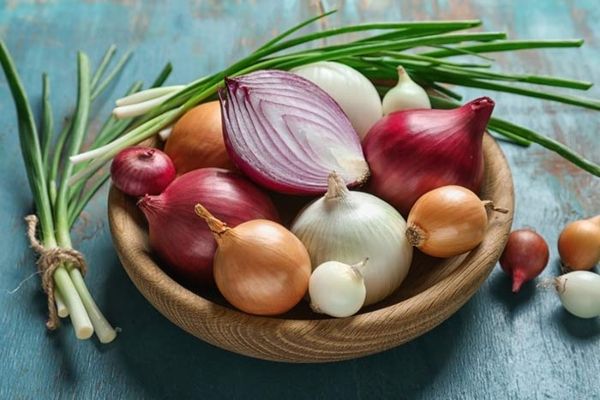 Ramas de cebollin y tazón de madera con cebollas de distintos tamaños y colores