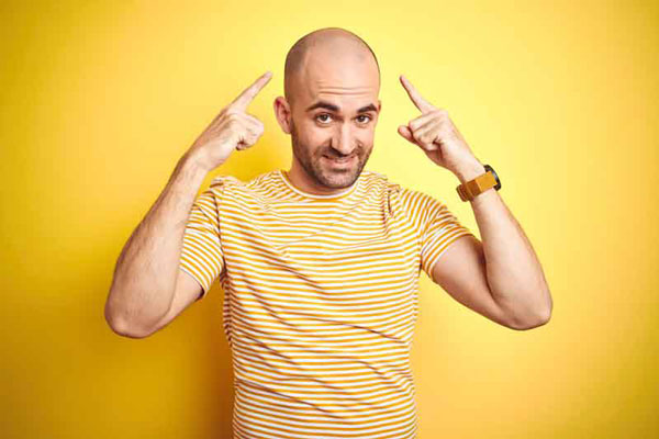 Alopecia en jóvenes - Hombre con camisa de rayas blancas y amarillas se muestra preocupado ante la pérdida de cabello en la parte superior de su cabeza
