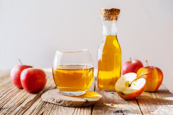 Vinagre de manzana - Imagen de un vaso con vinagre de manzana, junto a un recipiente con más líquido y varias manzanas rojas