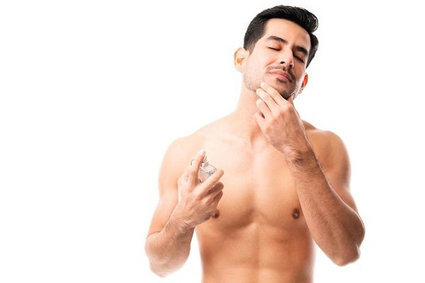 cuidar la barba - Hombre de cabello oscuro masajea su barbilla mientras se aplica perfume en el cuerpo 