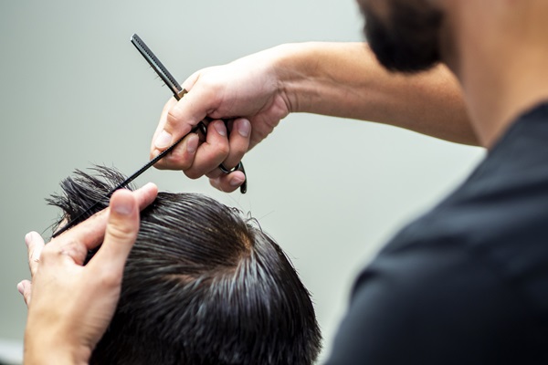 Estilista cortando el cabello de un hombre con una tijera, para tener más precisión y proteger los folículos pilosos implantados