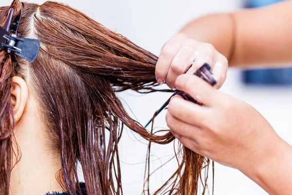 Tips para reparar el cabello dañado - Estilista separa el cabello de una clienta para nutrirlo e hidratarlo por partes