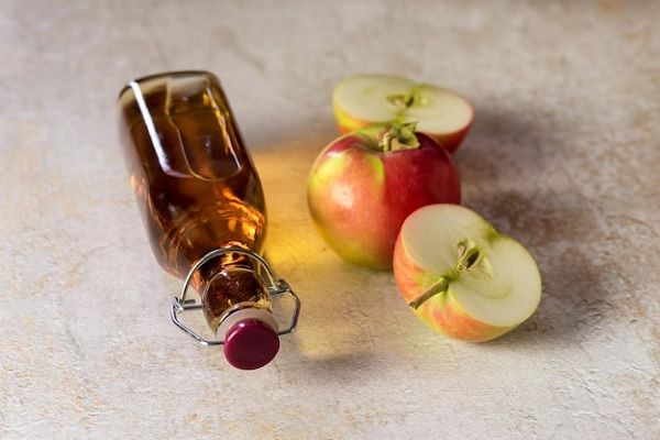 Vinagre de manzana - Imagen de un recipiente con vinagre de manzana al lado de varios ejemplares de la fruta