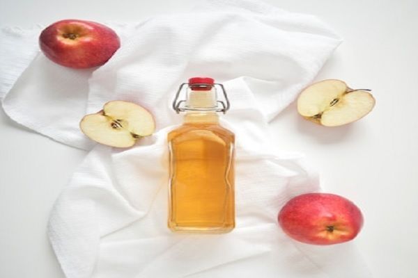 Vinagre de manzana - Imagen de un recipiente con vinagre de manzana, junto a las frutas de donde se extrajo el líquido