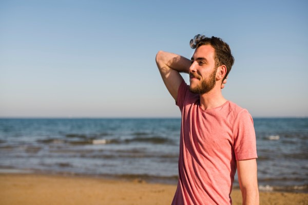 El sol daña el cabello - hombre sonriente con la mano en la nuca parado en la playa
