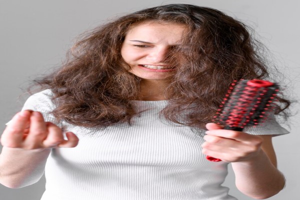 Alopecia androgénica en mujeres - mujer joven preocupada por el pelo que se ha quedado en el cepillo y el mechón que tiene en la mano