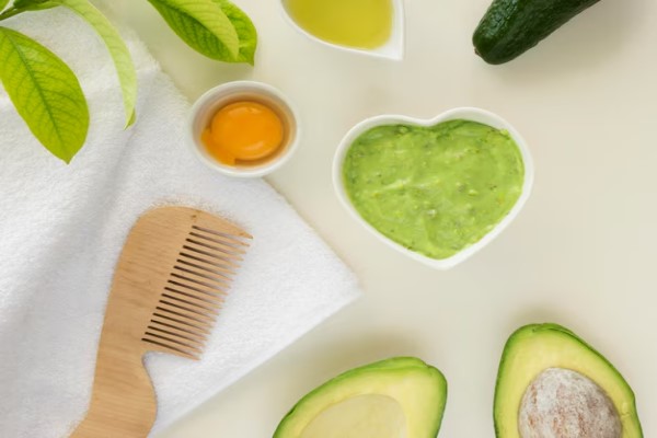 mascarilla de huevo y aguacate en un mesa al lado de los componentes y un peine de madera