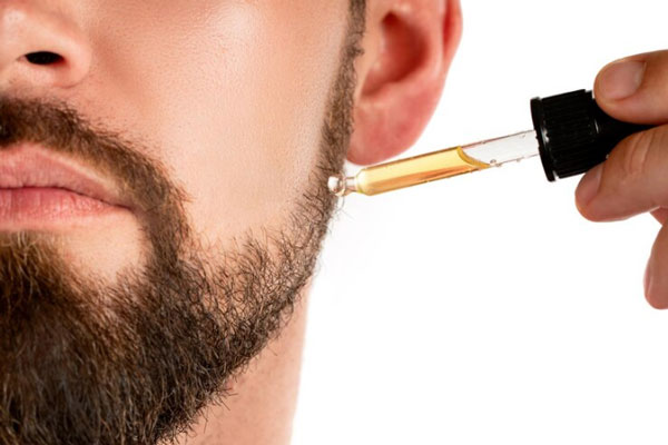 Cuidar la barba - Hombre sostiene un cuentagotas con aceites esenciales para potenciar el brillo y la nutrición de su barba