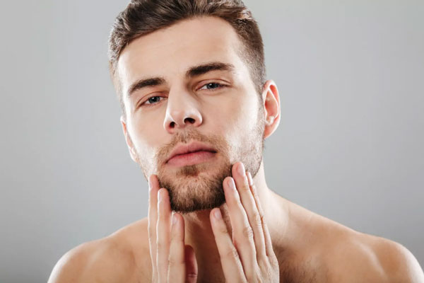 Cuidar la barba - Joven de tez clara se toca el rostro para evidenciar cuando a crecido su vello facial 