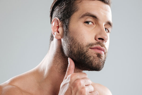 Hombre con abundante vello facial masajea su barbilla para mejorar la irrigación sanguínea en la zona 