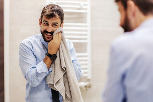 Cuidar la barba - Hombre con bigote y penacho seca su rostro con una toalla para retirar el exceso de humedad 