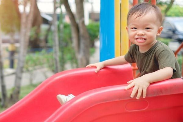 Alopecia en niños - niño con poca densidad capilar sentado en la parte superior de un tobogán
