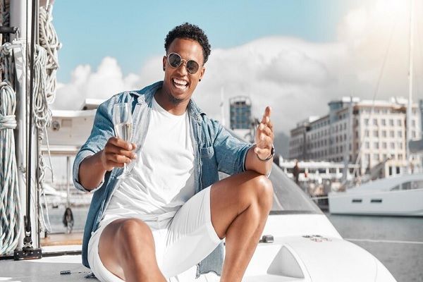 El sol daña el cabello - hombre sonriente sentado en la cubierta de un barco con una copa en la mano