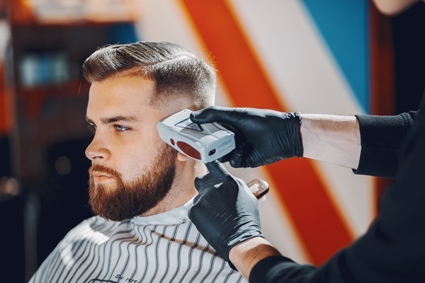 Estilista usa una máquina de afeitar para cortar el pelo de un hombre