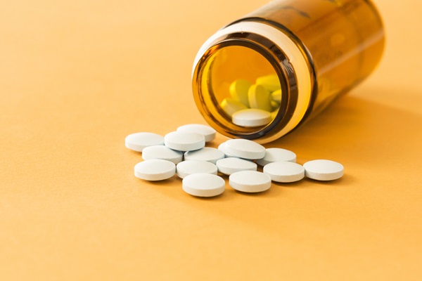 Espironolactona - Recipiente de pastillas blancas circulares derramadas sobre una mesa amarilla