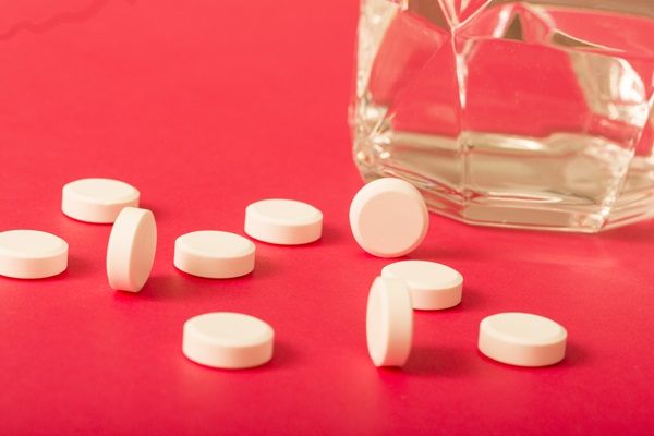 Espironolactona - Pastillas blancas circulares junto a un vaso de cristal sobre una mesa fucsia